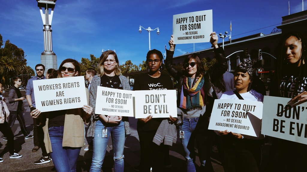 A photo of attendees at the Google walkout, carrying signs like 'Don't Be Evil'